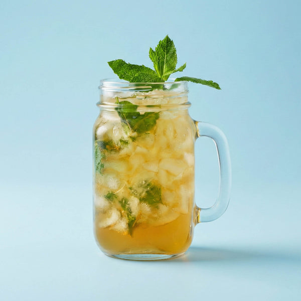 Glass mug with iced beverage and mint leaves on a light blue background