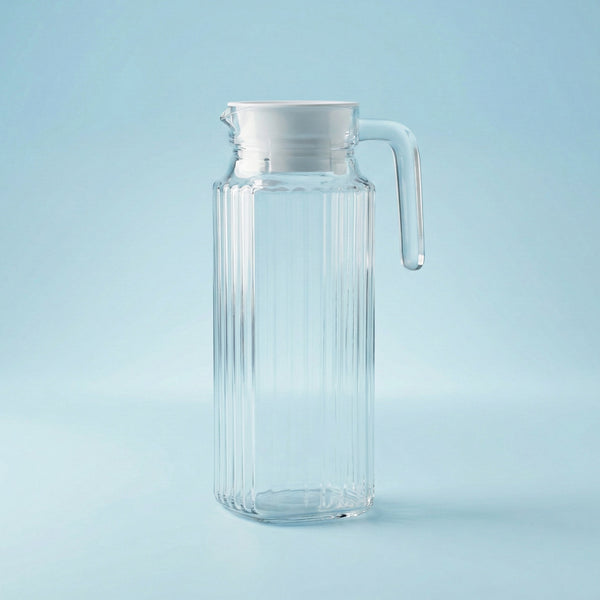 Clear glass pitcher with a handle on a light blue background